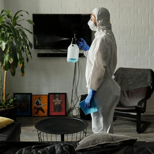 A person wearing PPE disinfects a living room for safety measures.